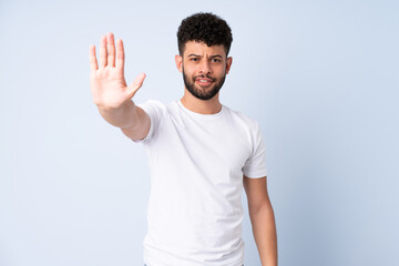 Young Moroccan man isolated on blue background making stop gesture