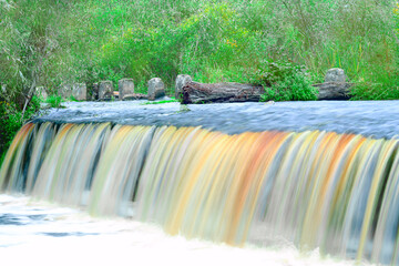 Small waterfall in the forest. Long exposure flow of water. Water casts with various colors. Peat water. 