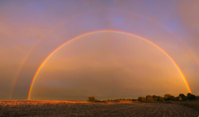 Fototapeta na wymiar Full double rainbow over autumn field in warm evening sunlight.