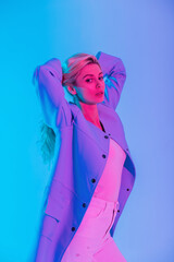 Fashion beauty girl model with stylish blue coat and white blouse with jeans indoors on colorful neon pink light