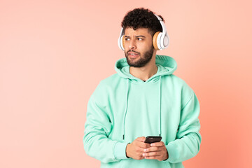 Young Moroccan man isolated on pink background listening music with a mobile and thinking
