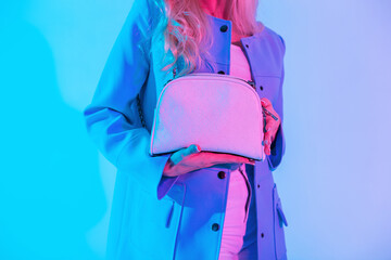 Stylish glamorous woman with a fashionable leather handbag in a blue jacket on colorful neon pink light in the studio. Girl holds white trendy bag