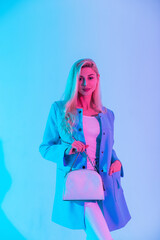 Fashionable beautiful business woman in bright elegant clothes and blazer holding a stylish white handbag in a studio with creative pastel light