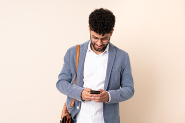 Young business Moroccan man isolated on beige background sending a message with the mobile
