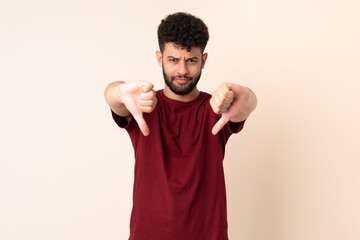 Young Moroccan man isolated on beige background showing thumb down with two hands