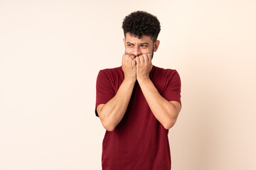 Young Moroccan man isolated on beige background nervous and scared putting hands to mouth