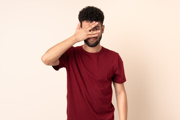 Fototapeta na wymiar Young Moroccan man isolated on beige background covering eyes by hands and smiling