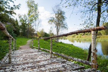 A wooden bridge made of birch logs on the bank of the river on a sunny day in the shade.