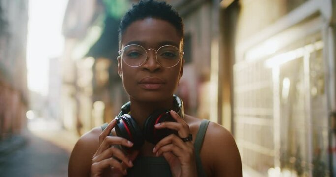 Portrait of stylish african girl with headphones in modern street. Beautiful young woman in fashion looking at camera outdoors.