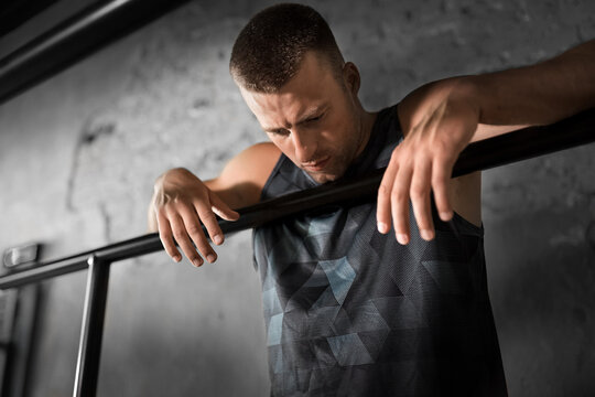 fitness, sport, training and lifestyle concept - tired young man exercising on parallel bars in gym