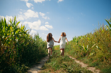 two girls holding hands run across the field in summer