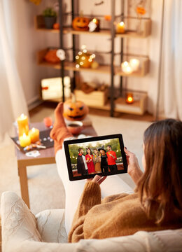 halloween, holidays and leisure concept - young woman looking at picture of frends in carnival costumes on tablet computer screen at home