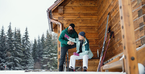 Mature couple resting by wooden hut outdoors in winter nature, cross country skiing.