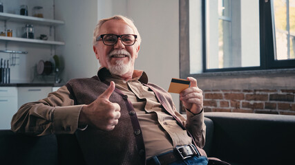 happy pensioner in eyeglasses holding credit card and showing thumb up