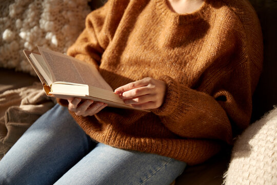 people, season and leisure concept - close up of woman in warm sweater reading book at home