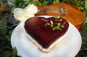 Heart shaped cake on a platter, a bouquet of white roses, a cup of coffee and a guitar.       