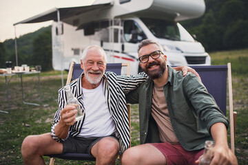 Mature man with senior father looking at camera at campsite outdoors, barbecue on caravan holiday trip.