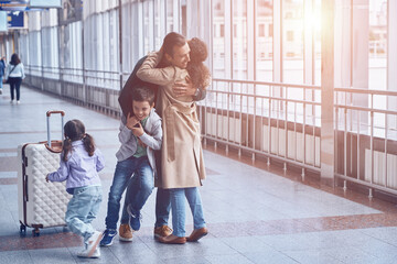 Full length of happy woman and two little kids meeting father at the airport