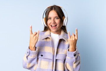 Young Lithuanian woman isolated on blue background listening music making rock gesture