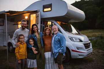 Portrait of multi-generation family looking at camera and smiling outdoors at dusk, caravan holiday trip. - obrazy, fototapety, plakaty