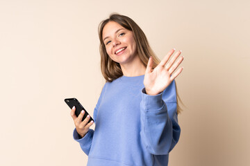 Naklejka premium Young Lithuanian woman using mobile phone isolated on beige background saluting with hand with happy expression