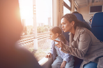 Beautiful mother with little daughter looking through a window while enjoying train journey together
