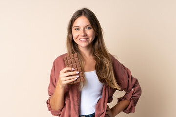 Young Lithuanian woman isolated on beige background taking a chocolate tablet and happy