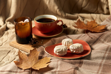 people, season and leisure concept - cup of coffee, autumn leaves, meringues and candle on warm blankets at home