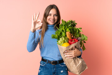 Young Lithuanian woman holding a grocery shopping bag showing ok sign with fingers