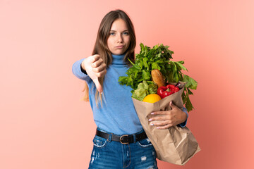 Young Lithuanian woman holding a grocery shopping bag showing thumb down with negative expression