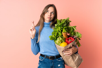 Young Lithuanian woman holding a grocery shopping bag with fingers crossing and wishing the best