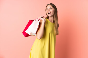 Fototapeta na wymiar Young Lithuanian woman isolated on pink background holding shopping bags and smiling