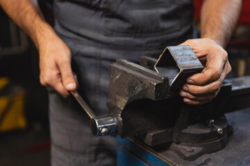 Close-up hands of male auto mechanic in dungarees with work tools working at car service station, indoors. Concept of labor, occupation, business, caree, job