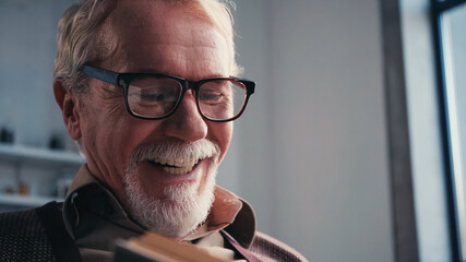 close up of happy senior man in eyeglasses reading book at home