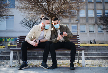 Men friends outdoors on street in town using smartphone, coronavirus and new normal concept.