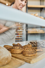 Close-up of woman in apron putting buns on display in bakery shop