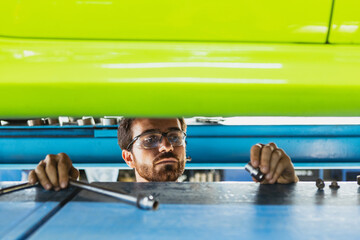 Close-up shot of young man, male auto mechanic in dungarees making car service at station, garage,...