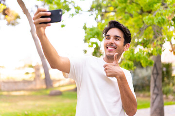 Young caucasian man in a park making a selfie with mobile phone