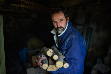 Fototapeta na wymiar Portrait of poor mature man holding firewood at home, looking at camera, poverty concept.