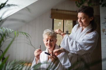 Happy senior mother in bathrobe with adult daughter indoors at home, selfcare concept.