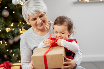 Fototapeta na wymiar christmas, holidays and family concept - happy grandmother and baby granddaughter opening gifts at home