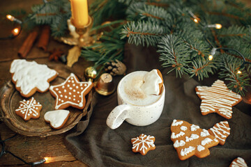 Christmas gingerbread cookies and coffee in stylish white cup, fir branches on napkin and rustic table. Christmas tree gingerbread cookie on coffee. Moody atmospheric image. Winter time