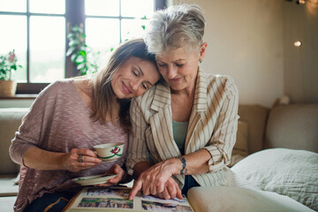 Front view of senior mother with adult daughter indoors at home, looking at family photographs.