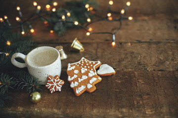 Fototapeta na wymiar Christmas gingerbread cookies, coffee cup, fir branches on background of warm lights on rustic wooden table. Atmospheric winter image. Seasons greeting. Merry Christmas