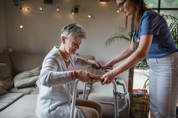 Fototapeta premium Healthcare worker or caregiver visiting senior woman indoors at home, helping her to walk.