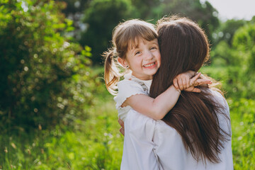 Caucasian young woman wearing white clothes have fun hugging child baby girl 5-6 years old. Mommy cuddle rest with little kid daughter spend time outdoor together. Mother's Day love family concept