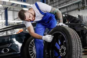 Fototapeta na wymiar Strong smiling happy young male professional technician car mechanic man 20s wears denim blue overalls white t-shirt stand hold check wheel work in light modern vehicle repair shop workshop indoors.