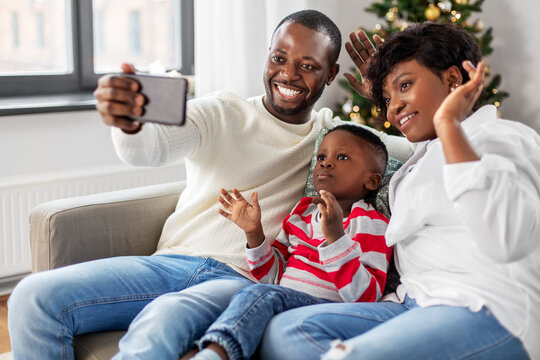 family, winter holidays and people concept - happy african american mother, father and little son taking selfie at home on christmas