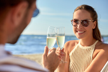 leisure, relationships and people concept - happy couple in sunglasses drinking champagne on summer beach