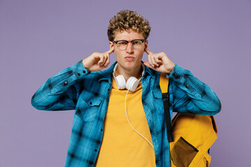 Young boy teen student in casual clothes backpack headphones glasses cover ears with hand finger do not want listen scream isolated on violet background studio Education in university college concept